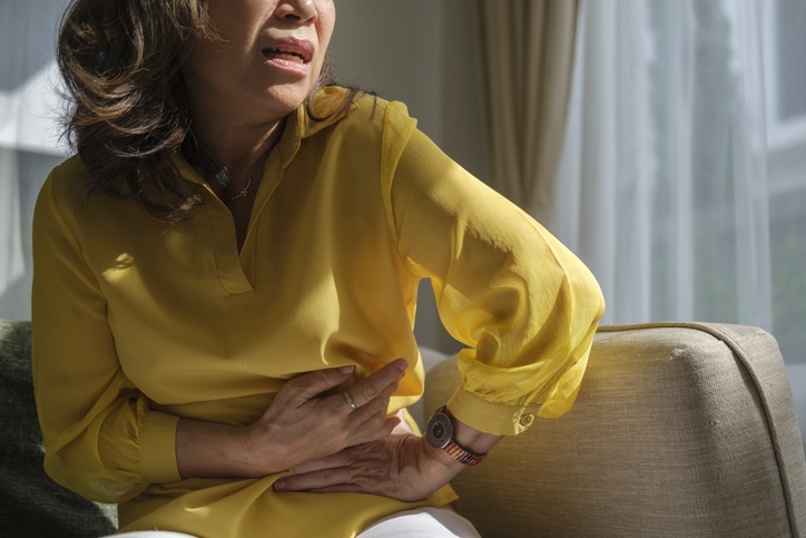 Women holding their abdomen while seated on a sofa, representing menopause discomfort in Maple Ridge
